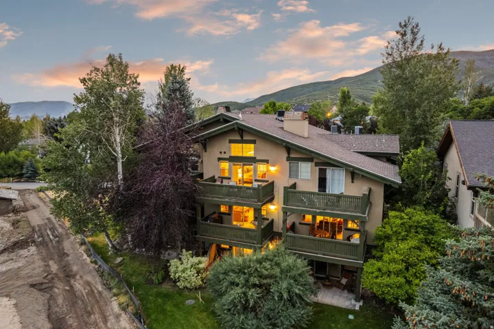 Multi-level residence featuring balconies with dark green railings, a stucco exterior, and a sloped roofline