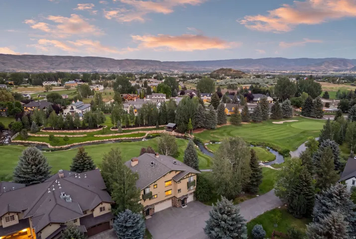Aerial view showcasing a residential area bordered by a golf course with a winding stream and mature trees