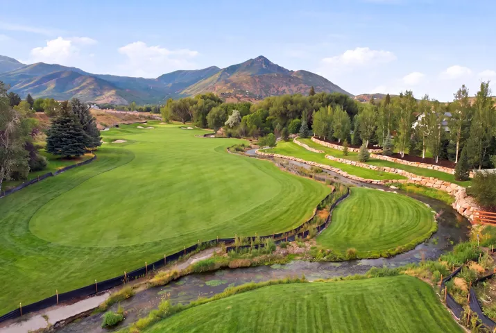 Expansive golf course featuring manicured fairways and natural water features, bordered by mature trees and mountain ranges