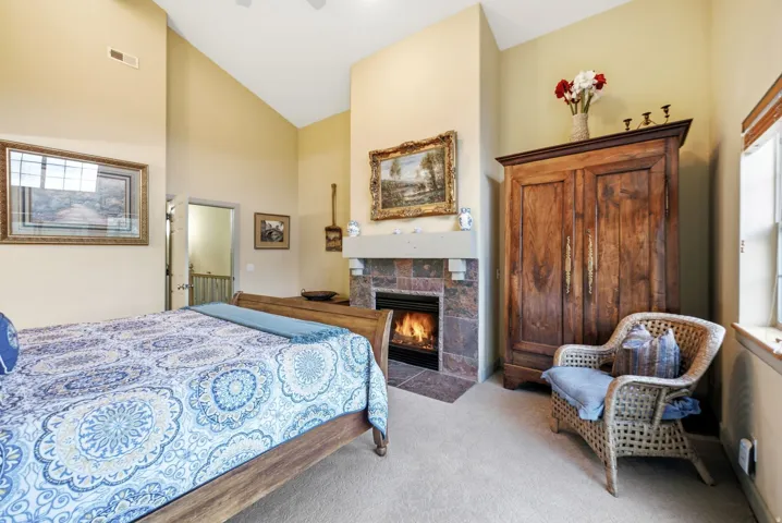 Vaulted ceiling bedroom with a stone-surround fireplace, mantle, and recessed lighting