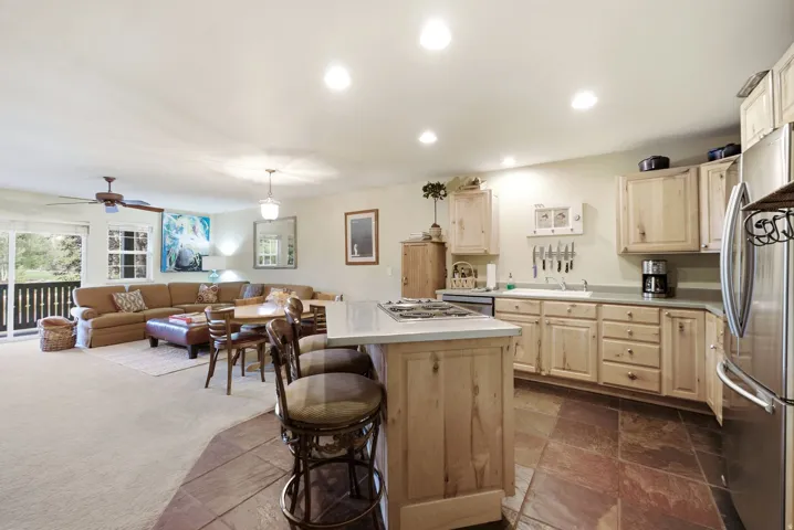 Open-concept kitchen featuring light wood cabinetry, a central island with a cooktop, and stainless steel appliances
