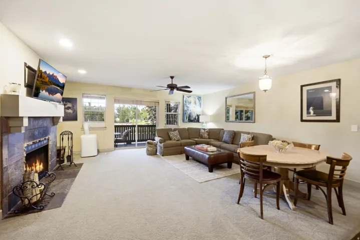 Spacious living area featuring a stone-faced fireplace with a white mantel, recessed lighting, and access to an outdoor balcony