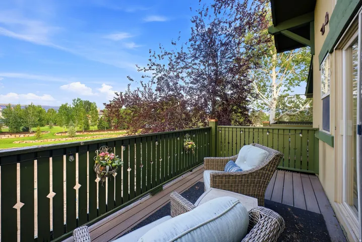 Outdoor balcony featuring composite decking, green painted wood railing, exterior lighting, and a sliding glass door