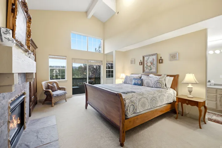 Spacious room featuring vaulted ceilings, a stone-clad fireplace with a hearth, carpeted flooring, and a sliding glass door opening to an outdoor deck
