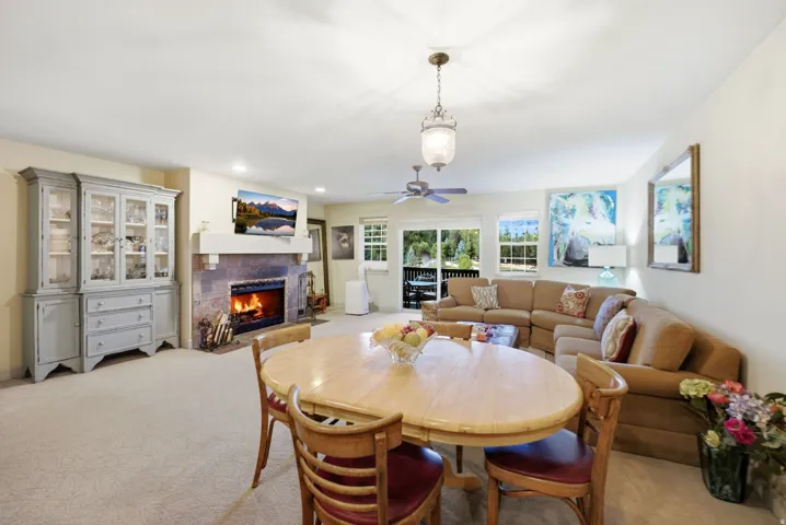 Open-concept living space with a stone-surround fireplace, light-toned carpet flooring, and a sliding glass door providing exterior access