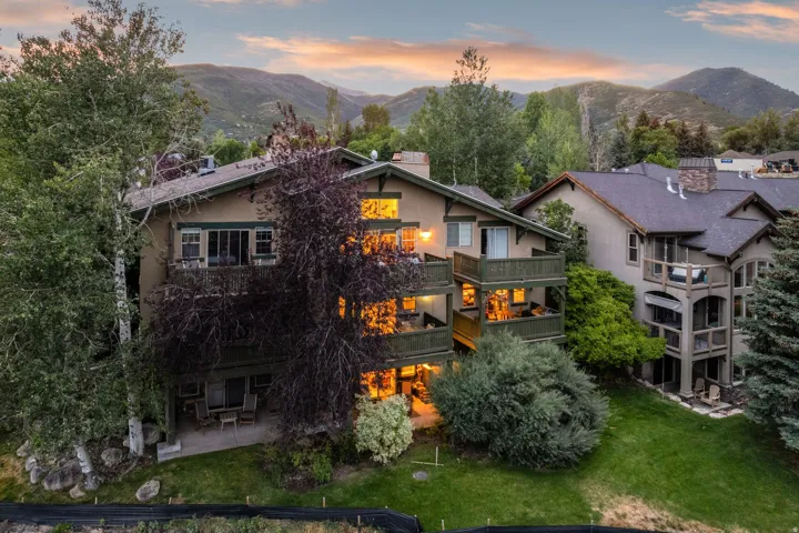 Multi-level stucco exterior featuring multiple balconies, a ground-level patio, and surrounding mature trees
