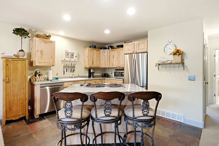 Kitchen featuring natural wood cabinetry, stainless steel appliances, a center island with a cooktop, stone-finish flooring, and recessed lighting