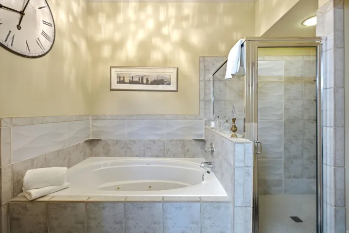 Corner soaking tub and a glass-enclosed shower featuring tile surrounds