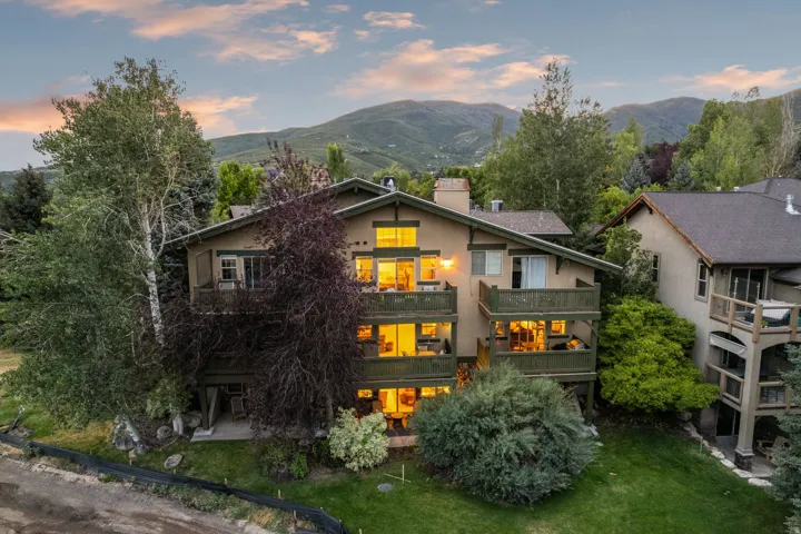 Multi-story residence featuring extensive balconies, a stucco and wood exterior, and a prominent mountain backdrop