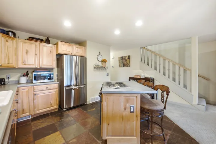 Kitchen featuring natural wood cabinetry, stainless steel refrigerator, dark tiled flooring, recessed lighting, and a kitchen island with cooktop