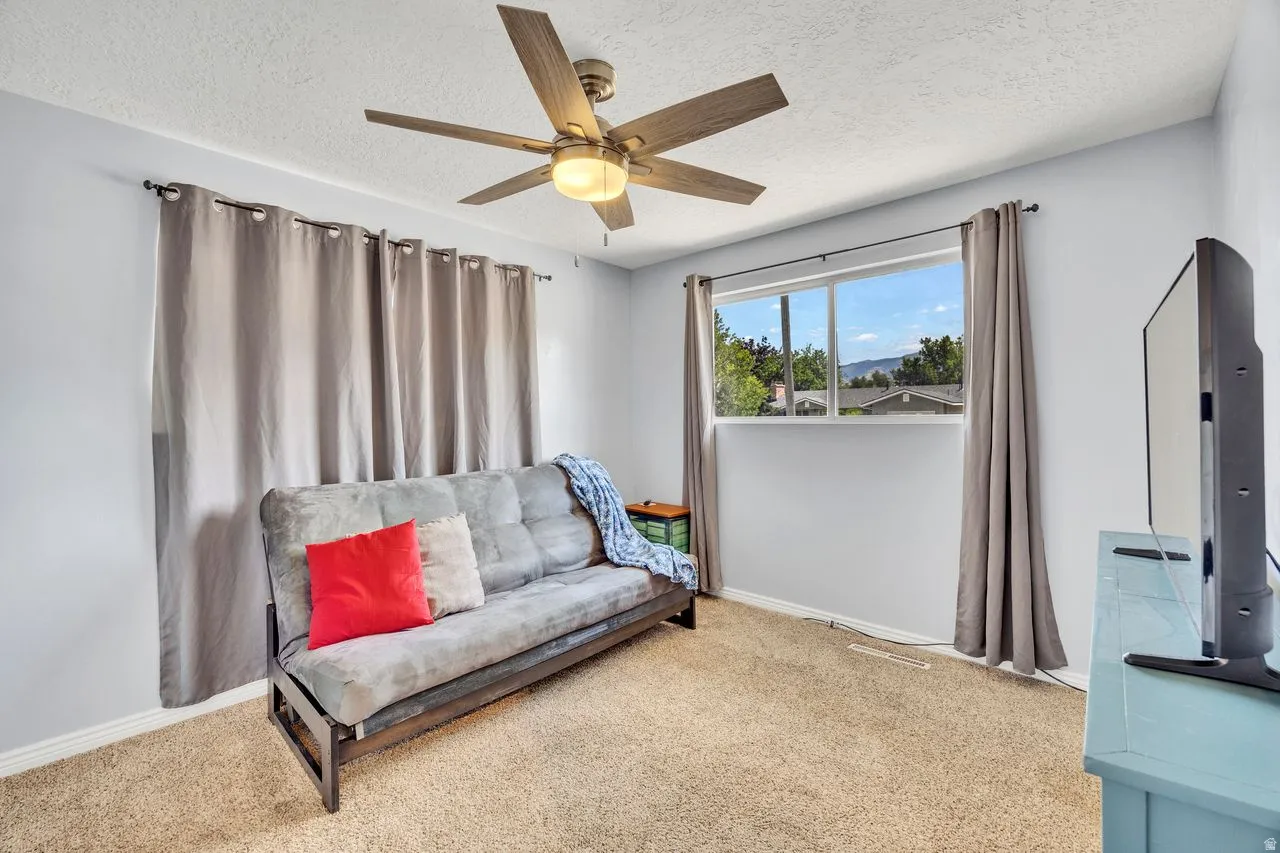 Bright room featuring a ceiling fan with integrated lighting, a large window, light-colored walls, and carpeting