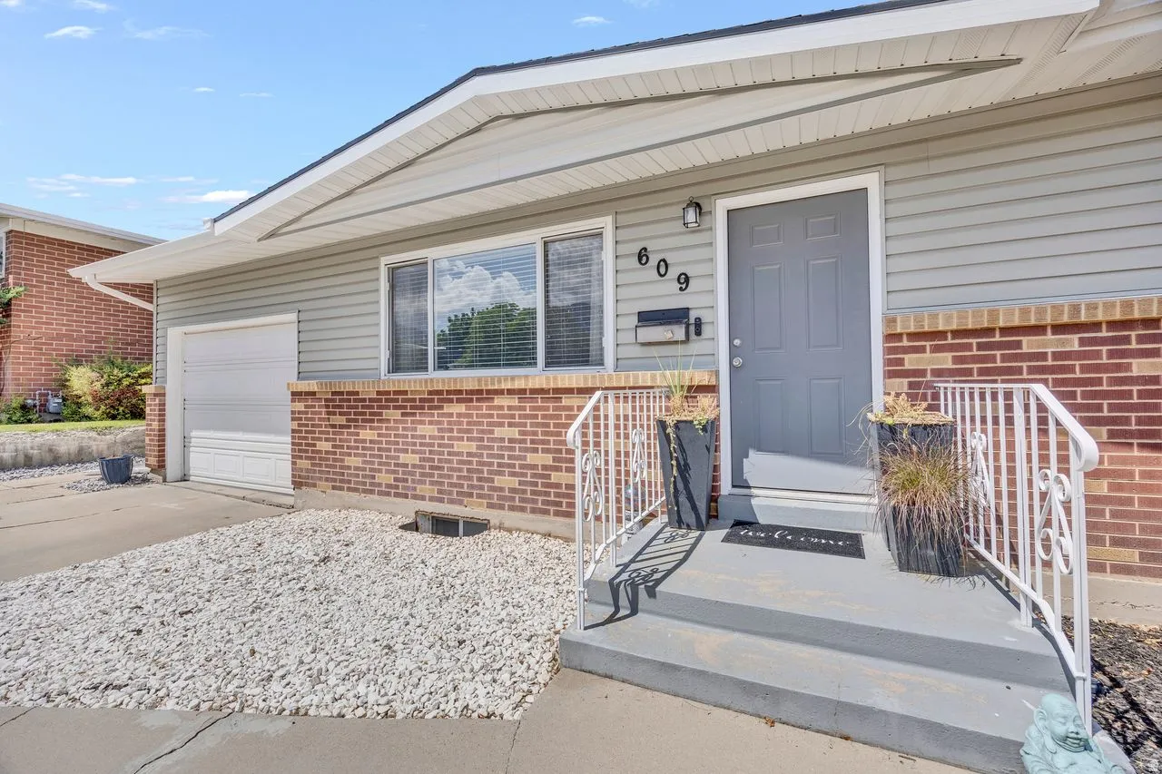 Exterior featuring light gray siding, brick accents, white window trim, and a gray front door