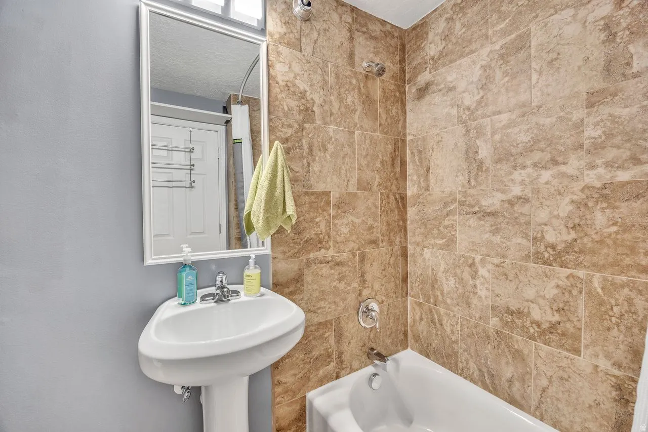 Bathroom featuring a pedestal sink, framed wall mirror, and a bathtub with a tiled shower surround