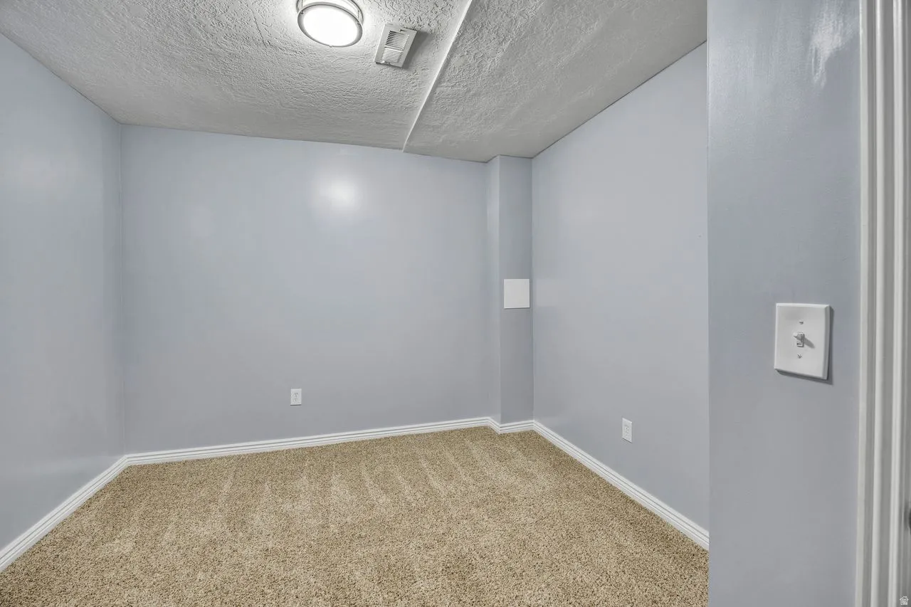 Carpeted room featuring light gray walls, white baseboards, and a textured ceiling