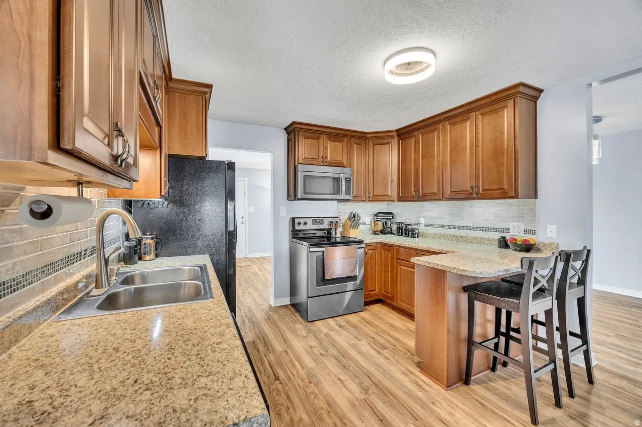 Kitchen featuring wood-finish cabinetry, granite countertops, stainless steel appliances, a double basin sink, and wood-finish flooring