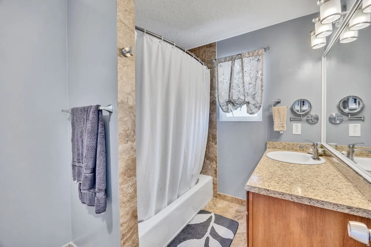 Bathroom featuring a tub/shower combination with tile surround, a single vanity with stone-finish countertop, and wall-mounted lighting fixtures