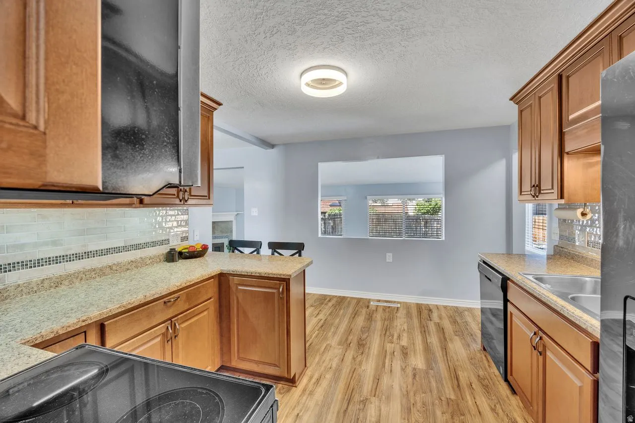 Kitchen featuring wood-finish flooring, warm wood cabinetry, light-toned countertops, and a subway tile backsplash