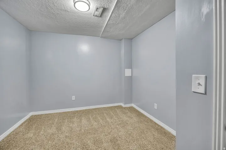 Carpeted room featuring light gray walls, white baseboards, and a textured ceiling