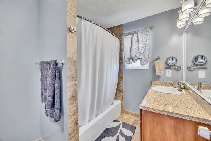Bathroom featuring a tub/shower combination with tile surround, a single vanity with stone-finish countertop, and wall-mounted lighting fixtures