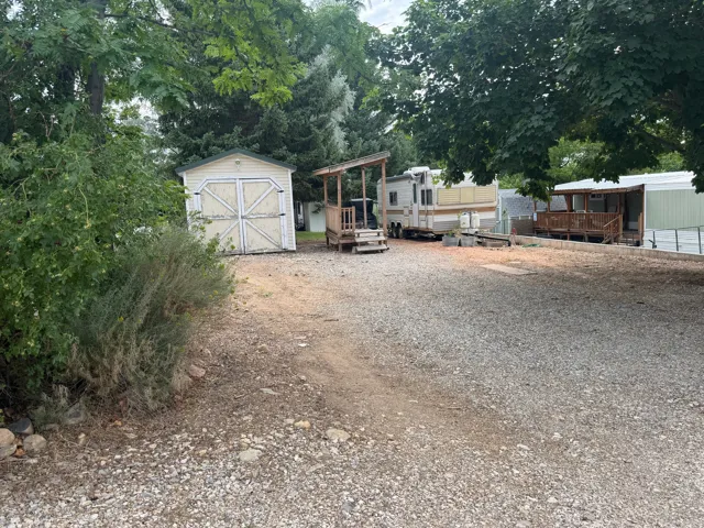 Gravel driveway with ample parking space, featuring a storage shed, established trees, and natural landscaping