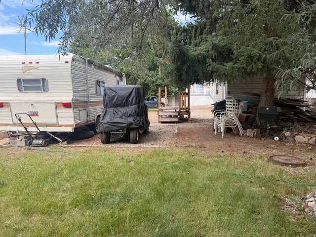 Gravel parking area featuring a covered vehicle, a travel trailer, and a manicured lawn area