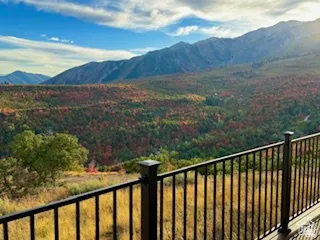 Expansive mountain landscape with diverse foliage, captured from a deck featuring dark metal railings and a composite deck surface