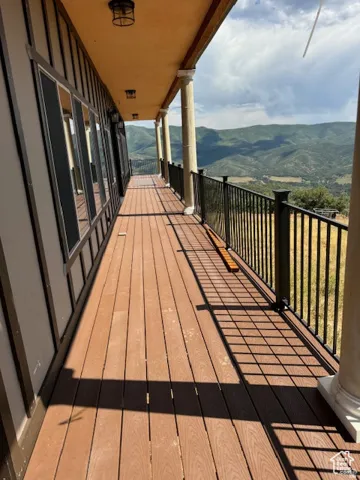 Expansive outdoor deck featuring wood-finish flooring, a black metal railing, and decorative architectural columns