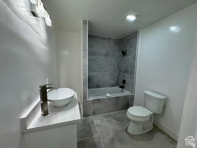 Contemporary bathroom featuring a vessel sink with a tall chrome faucet, a white vanity with a light-toned countertop, a built-in tub with dark gray tile surround, and coordinating large format floor tiles