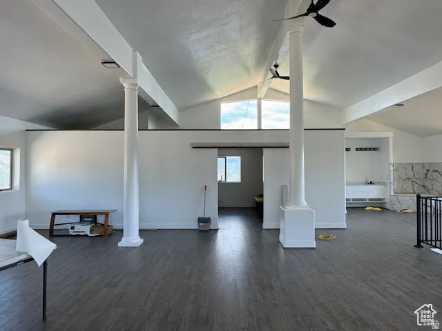 Expansive interior space featuring vaulted ceilings, wood-finish flooring, architectural columns, and a built-in wet bar with a stone-look backsplash