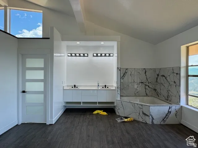 Spacious bathroom featuring a built-in tub with marble-patterned tile surround, dual vanity with modern cabinetry, wood-finish flooring, and a contemporary door with frosted glass panels