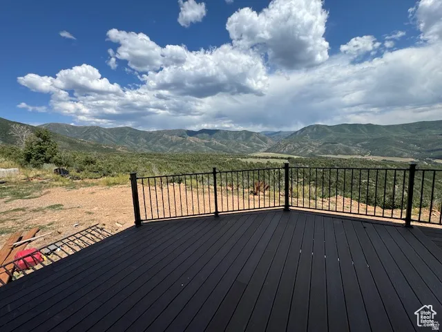 Spacious outdoor deck with dark composite decking and black metal railings, overlooking extensive mountainous terrain and natural landscaping