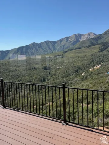 Outdoor deck with wood-finish flooring and a black metal railing, overlooking a mountainous landscape with abundant greenery