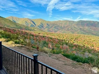 Expansive mountain and tree-filled scenery, with a black metal railing and deck visible in the foreground