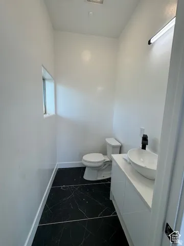 Modern powder room featuring black marble-look tile flooring, a white vessel sink atop a sleek white vanity, a contemporary black wall-mounted faucet, and a narrow window for natural light