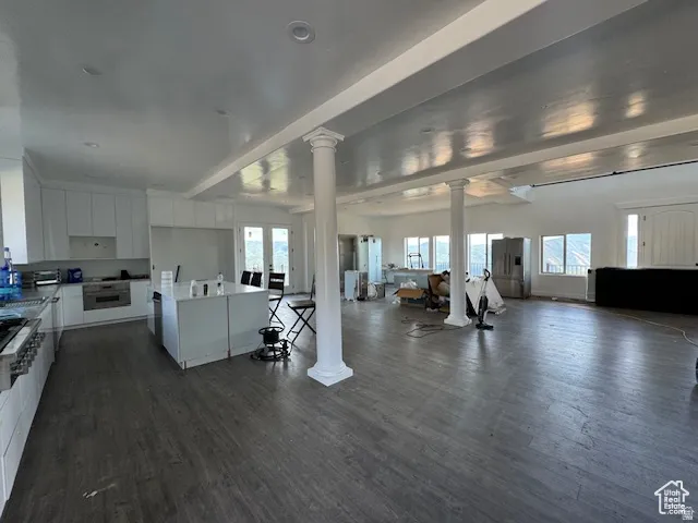 Open-concept interior featuring wood-finish flooring, white cabinetry, recessed lighting, and decorative columns