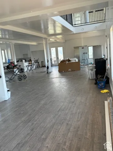 Spacious open-concept living area featuring wood-finish flooring, white walls, and a multi-level design with an upper-level balcony