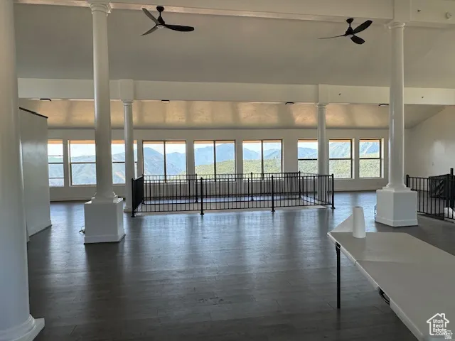 Spacious room featuring multiple large windows showcasing mountain scenery, wood-finish flooring, two ceiling fans, and decorative columns