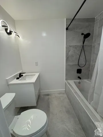 Bathroom featuring a modern floating vanity with a white countertop and rectangular sink, matte black fixtures, a contemporary wall-mounted light fixture, a tiled shower/tub combination with matte black hardware, and coordinating large format floor tiles