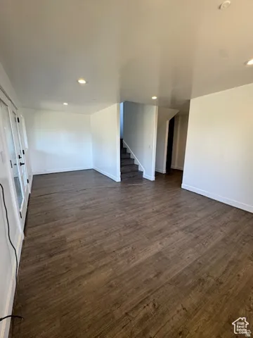 Spacious room with wood-finish flooring, white walls, recessed ceiling lighting, and a staircase with carpeted treads