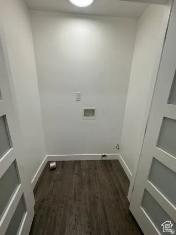 Dedicated laundry area featuring modern doors with frosted glass panels, wood-finish flooring, a wall-mounted light fixture, and essential utility connections
