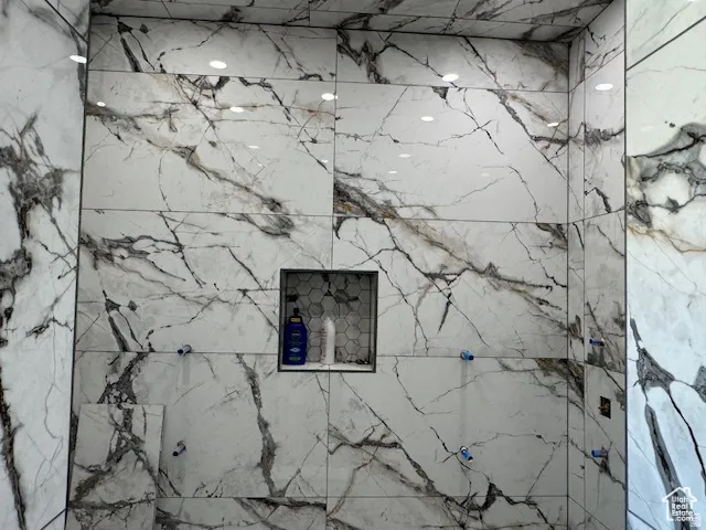 Spacious shower enclosure featuring large format porcelain tile with extensive veining, a built-in hexagonal tile niche, and recessed ceiling lighting