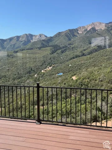 Outdoor deck featuring wood-finish flooring and a black metal railing, overlooking a mountainous landscape with abundant tree coverage