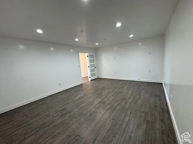 Spacious room featuring wood-finish flooring, recessed lighting, white walls, and a contemporary door with frosted glass panels