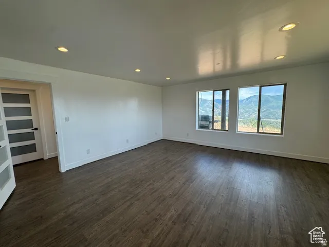 Spacious room featuring wood-finish flooring, recessed lighting, and two large windows showcasing a mountain backdrop