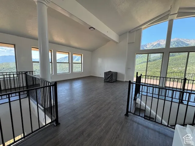 Spacious loft with vaulted ceilings, large picture windows, wood-finish flooring, and black metal railings overlooking a mountain landscape