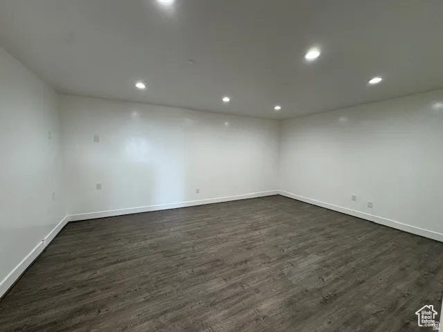 Spacious room featuring wood-finish flooring, white walls, recessed ceiling lighting, and white baseboards