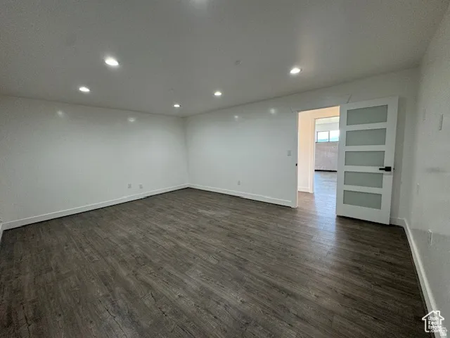 Spacious room featuring wood-finish flooring, white walls, recessed ceiling lighting, and a modern five-panel door with frosted glass inserts and matte black hardware