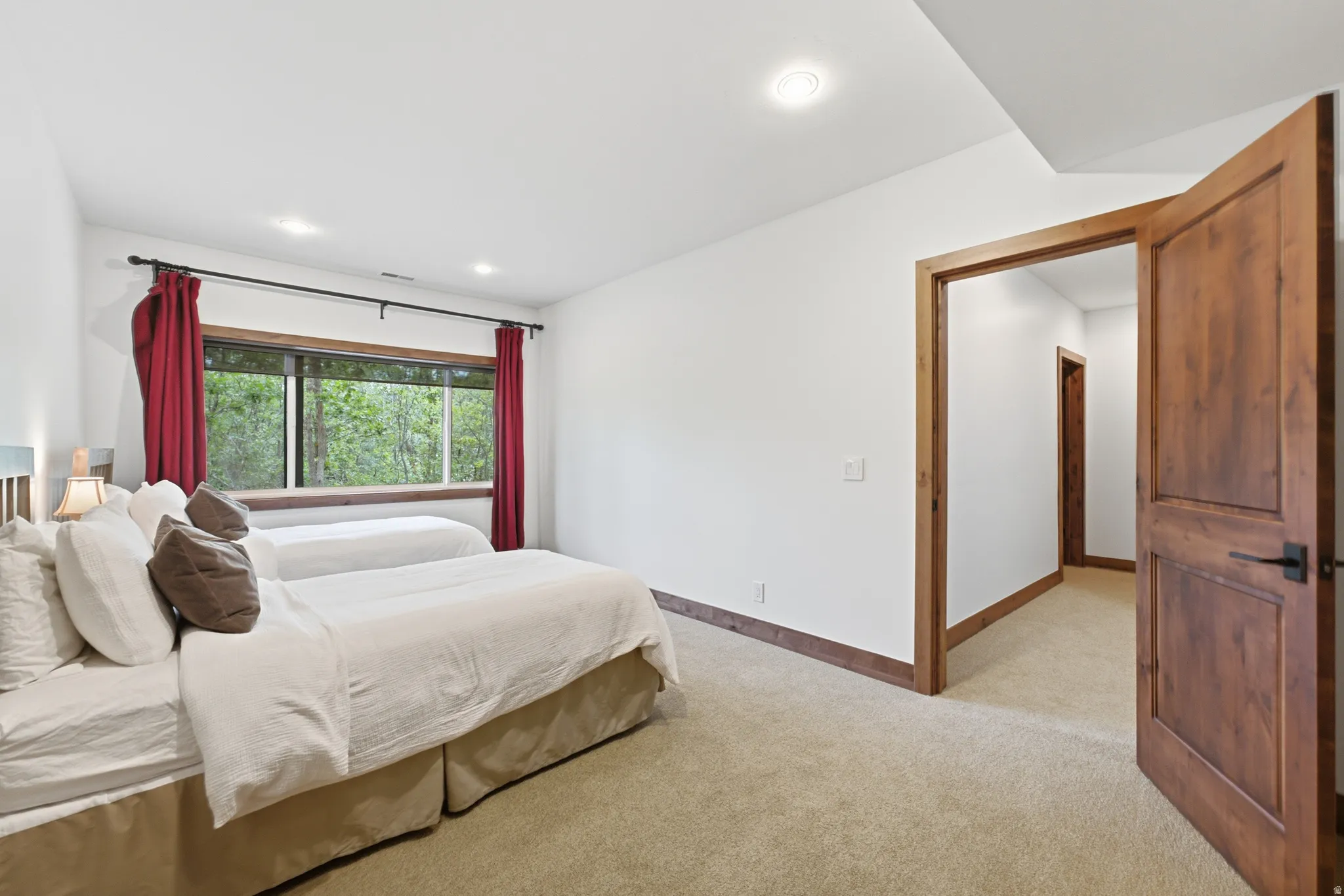 Carpeted room with a wide window framing lush greenery, recessed lighting, white walls, and a wood-paneled door