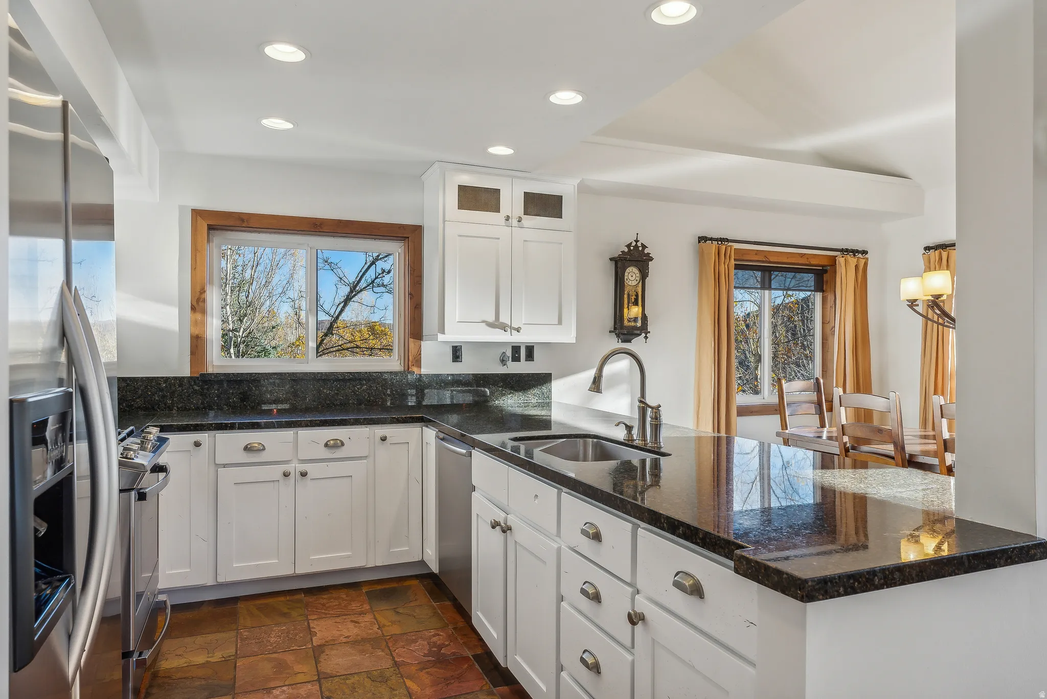 Kitchen featuring dark stone countertops, white cabinetry, integrated stainless steel appliances, a double basin sink with a high-arc faucet, and recessed lighting