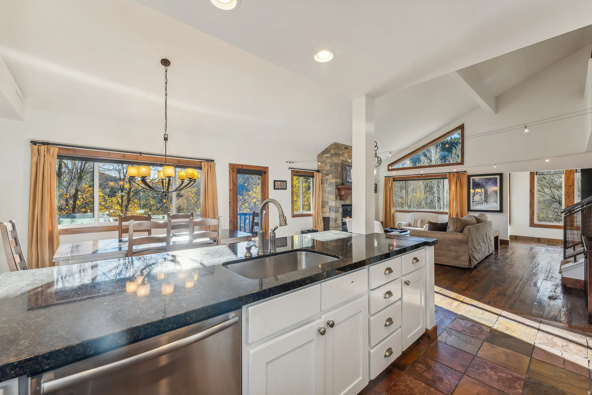 Kitchen island with granite countertop and undermount sink, stainless steel dishwasher, white cabinetry, and wood-finish flooring